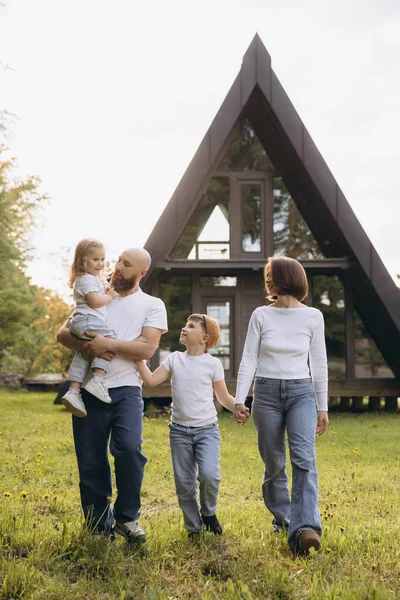 Happy family walking on grass in front of their modern a frame house, enjoying a sunny day together