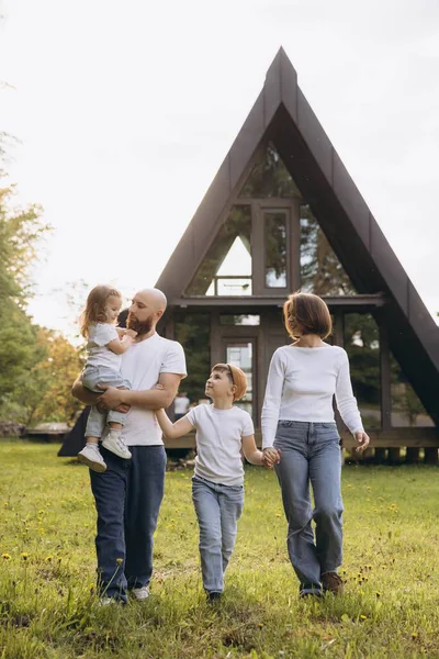 Happy family enjoying a walk on the grass in front of their contemporary a frame house, embracing the joys of togetherness and modern living