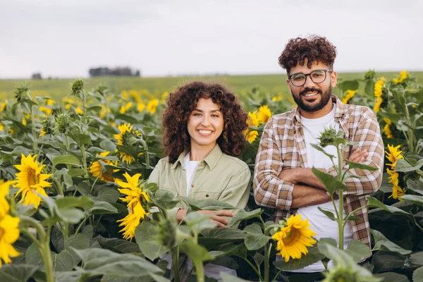 Two agronomists smiling with crossed arms while enjoying a sunny day in a vibrant sunflower field, embodying the essence of rural agriculture