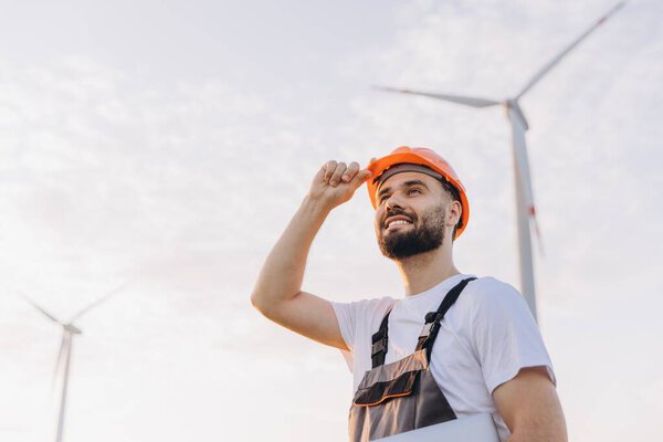 Smiling engineer adjusting his helmet while working on a wind turbine, contributing to the advancement of renewable energy solutions