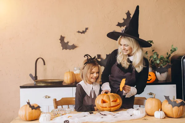 Mother in a witch costume guiding her daughter while carving a pumpkin for a festive Halloween party, creating joyful family memories together