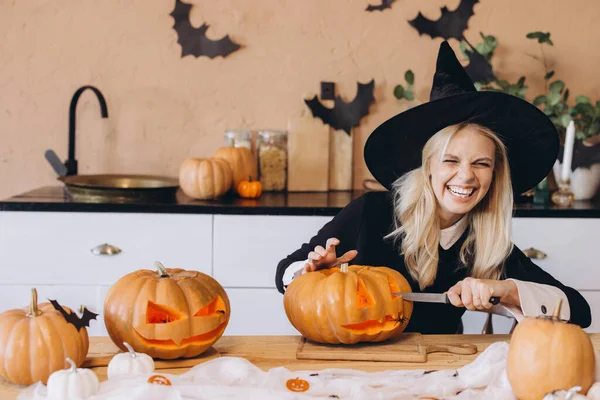 Young woman with a witch hat happily carving pumpkins for a Halloween party in a cozy kitchen, embracing festive autumn traditions