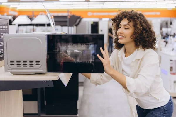 Smiling woman checking microwave oven, shopping for kitchen appliances in home appliance store