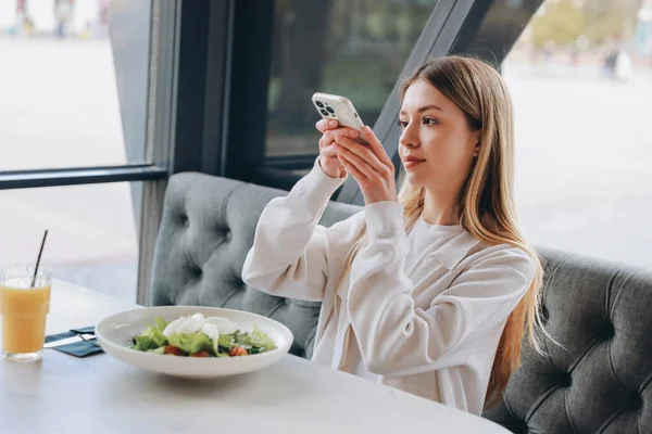 Customer photographing her lunch with smartphone in modern restaurant, enjoying healthy meal and sharing on social media