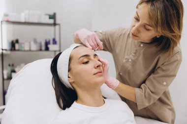 Beautician performing botox injection treatment on forehead of woman lying on couch in beauty clinic