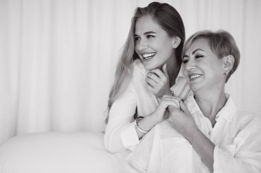 Happy mother and daughter are laughing and holding hands, wearing white shirts, in a black and white portrait
