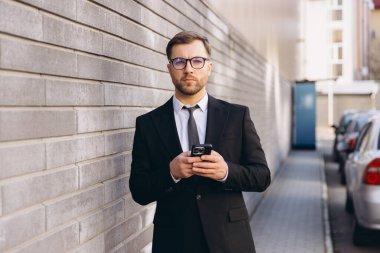Businessman wearing suit and tie using smartphone standing next to a brick wall in the city