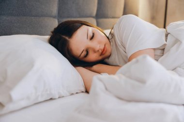 Young woman resting in bed with white sheets and pillows, enjoying a peaceful and comfortable sleep