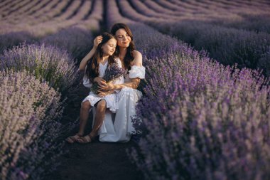 Mother and daughter wearing flowing white dresses, embracing joyfully amidst a stunning lavender field, surrounded by vibrant blooms