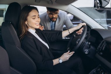 Businesswoman testing a new car in a dealership, engaging with a salesman who is expertly showcasing the vehicle's features and benefits