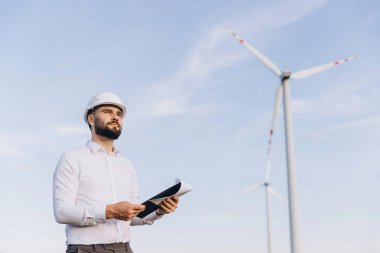 Engineer holding blueprints inspecting the construction of wind turbines in a wind farm for sustainable energy production