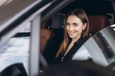 Saleswoman smiling while sitting inside a new car at the dealership, promoting the automotive industry and car sales business