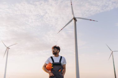 Arab engineer holding helmet inspecting wind turbines in the desert for renewable energy production