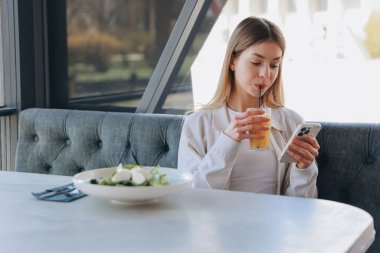 Businesswoman enjoying a healthy lunch while browsing her smartphone in a stylish, modern cafe filled with natural light