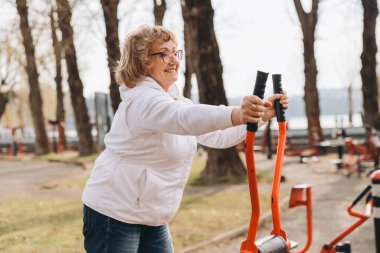 Elderly person enjoying healthy lifestyle, working out in a park equipped with fitness machines