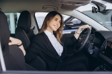 Businesswoman smiling while testing a new car in a dealership, confidently gripping the steering wheel, enjoying the experience