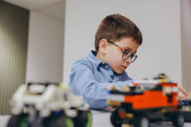 Young boy wearing glasses concentrating on building toy car at home using colorful construction blocks