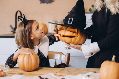 Mother and daughter having fun carving pumpkins for Halloween party, wearing Halloween costumes