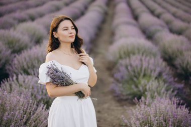 Beautiful model enjoying a sunny day in a lavender field, holding a bouquet of freshly picked lavender flowers