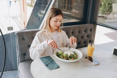Businesswoman eating fresh salad with mozzarella cheese and drinking orange juice in a restaurant during her lunch break