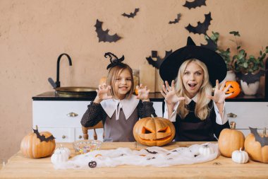 Mother and daughter sharing laughter while creating funny faces and preparing carved pumpkins for an exciting Halloween party