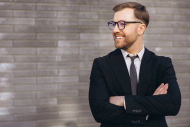 Portrait of a confident businessman smiling with crossed arms near a gray brick wall