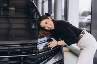Woman joyfully hugging car in a modern dealership showroom