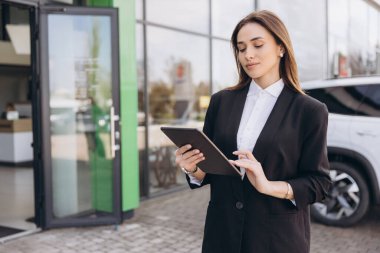 Saleswoman engaging with customers using a digital tablet at a car dealership, facilitating the buying and selling of vehicles