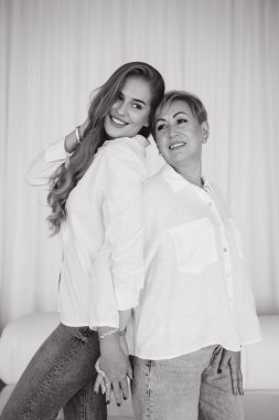 Black and white portrait of a happy mother and daughter holding hands and smiling, wearing white shirts and jeans