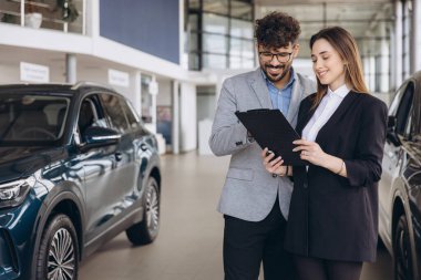 Salesman and client reviewing a contract inside a car dealership, engaging in discussions about purchasing a new vehicle