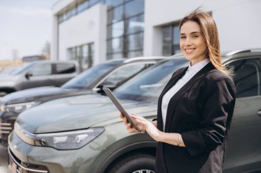 Saleswoman smiling and using tablet while working at car dealership