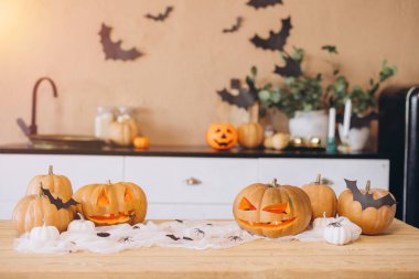 Cadılar Bayramı kutlamaları için mutfakta ahşap bir masa süsleyen ürkütücü yüzler ve kağıt yarasalarla oyulmuş balkabakları.