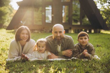 Happy family lounging on the grass, soaking up the sun and enjoying quality time together during a vacation at a modern a frame cabin