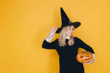 Young woman in a witch costume joyfully holding a carved pumpkin, celebrating Halloween with a festive and cheerful spirit