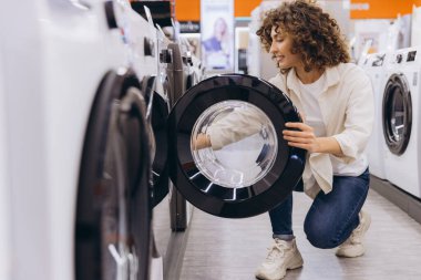 Young woman checking washing machine drum in home appliance store, choosing new washer for her apartment