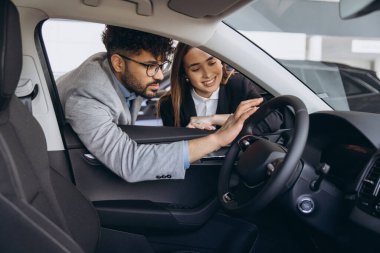 Saleswoman engaging with a customer, highlighting features of a new car inside a modern dealership showroom, fostering a confident buying experience