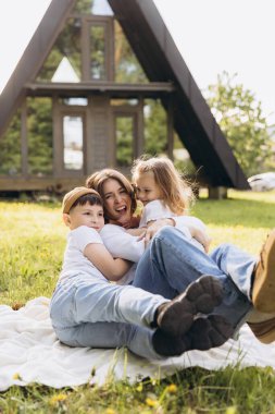 Mother and children enjoying leisure time together, embracing on a blanket in front of their modern a frame house, expressing love and happiness