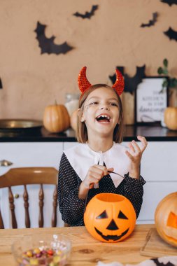 Little girl laughing and wearing devil horns holding a pumpkin basket for trick or treat, celebrating Halloween