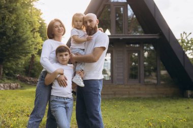 Happy family smiling together in front of their modern a frame house, enjoying a sunny day filled with laughter and love in the garden