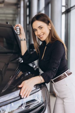 Saleswoman holding car keys and caressing a car in a dealership
