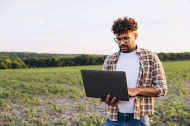 Agronomist using laptop while inspecting crops in a soybean field, implementing modern agriculture techniques