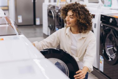 Smiling woman selecting a new washing machine while browsing through a variety of options in a retail store dedicated to home appliances