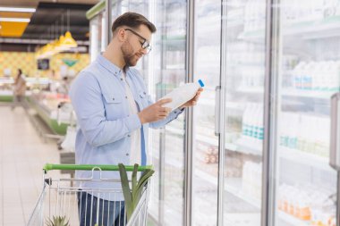 Man choosing a bottle of milk in refrigerated section at grocery store
