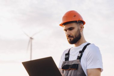 Engineer is working on a laptop in a wind turbine farm, symbolizing the transition to sustainable energy