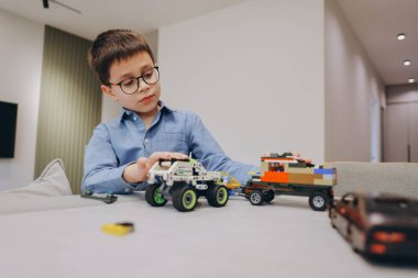 Smart kid wearing glasses playing with building blocks, developing his creativity and problem solving skills in a playful home environment