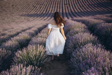 Model gracefully walking through vibrant rows of lavender, wearing a stunning white dress, embodying beauty and tranquility in nature's embrace