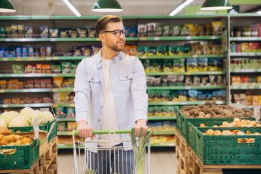 Customer pushing shopping cart and choosing products in supermarket