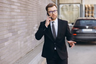Businessman in suit making a phone call while walking on the street near office building