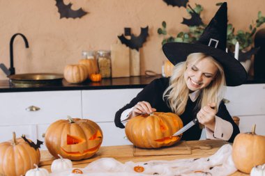 Young woman carving a pumpkin for Halloween, dressed in a witch costume and beaming with joy in her cozy kitchen