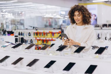 Customer choosing smartphone in consumer electronics store, comparing mobile phones on display